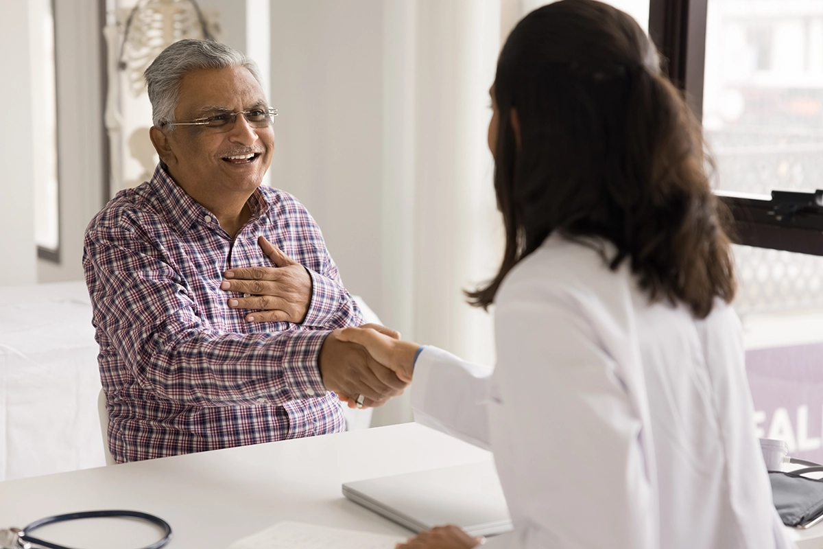 A health practitioner shaking hands with a patient across a desk in a clinical setting.